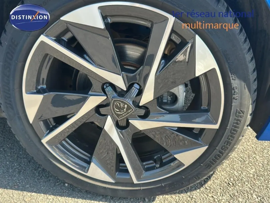 Gros plan sur la jante alliage 17 pouces noire et argentée d'une Peugeot 308 bleu clair, avec logo Peugeot central.