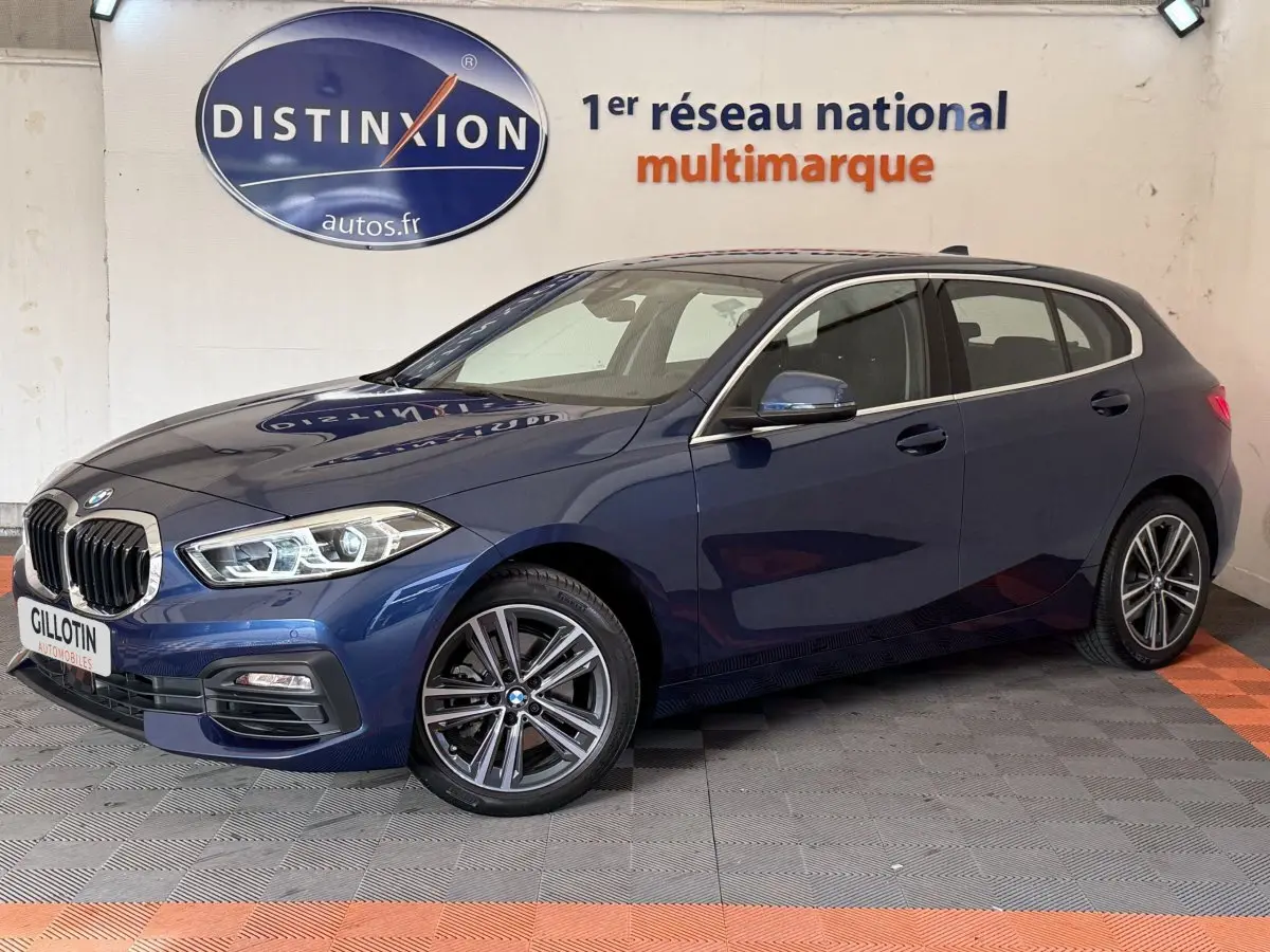 BMW Série 1 116i Business Design bleu vue 3/4 avant droit, avec jantes alliage et phares LED ellipsoïdaux.