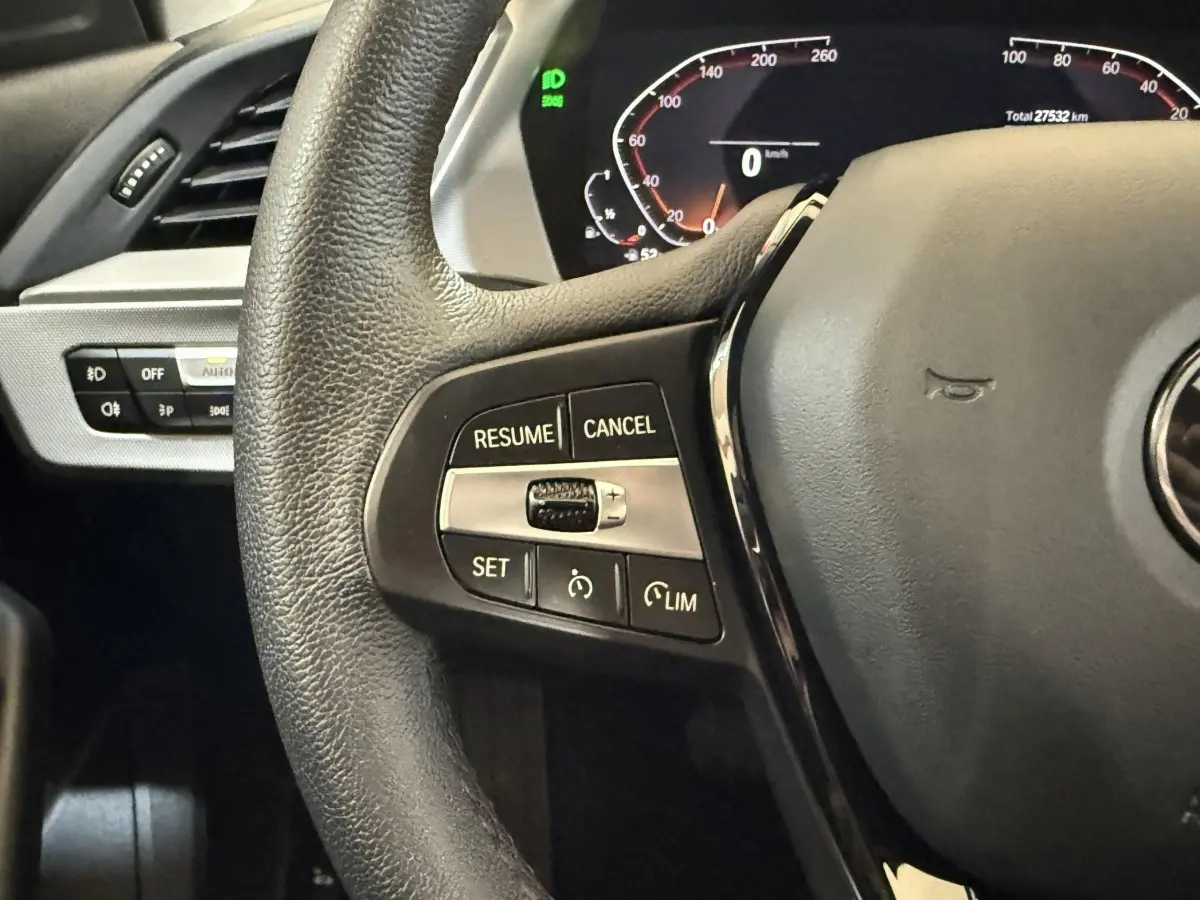 Gros plan sur le volant cuir noir de la BMW Série 1 116i avec commandes de régulateur de vitesse et tableau de bord digital.