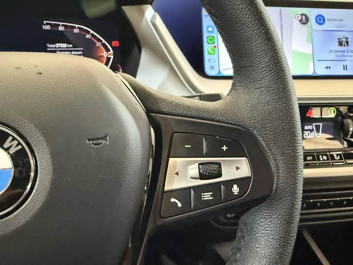 Gros plan sur le volant cuir noir de la BMW Série 1 116i 2023 avec commandes multifonctions et tableau de bord digital.