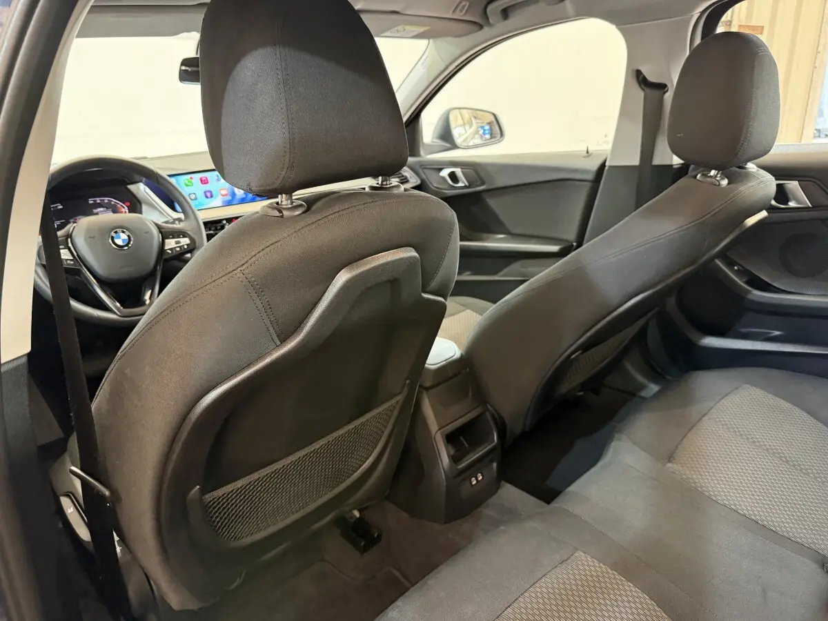 Vue intérieure arrière de la BMW Série 1 116i bleu, montrant les sièges tissu et le tableau de bord avec écran tactile.
