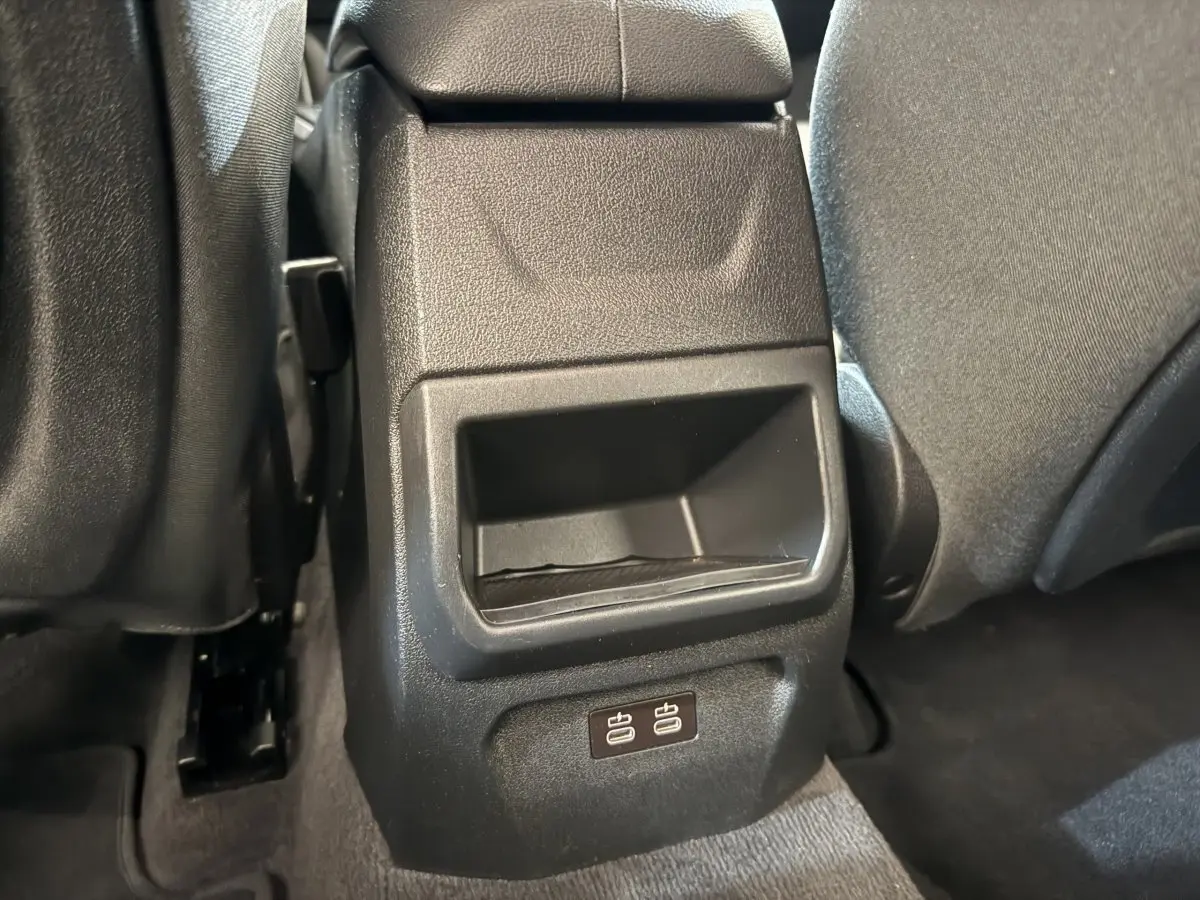 Gros plan sur la console arrière noire avec deux ports USB, entre les sièges tissu gris foncé d'une BMW Série 1 bleue.