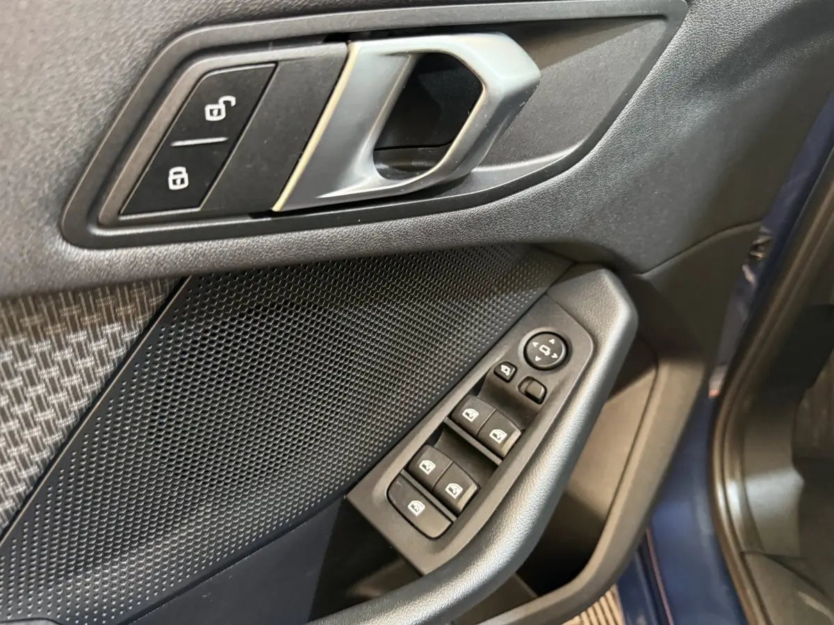Gros plan sur la porte avant gauche bleu d'une BMW Série 1 116i, montrant les commandes des vitres et la poignée intérieure.