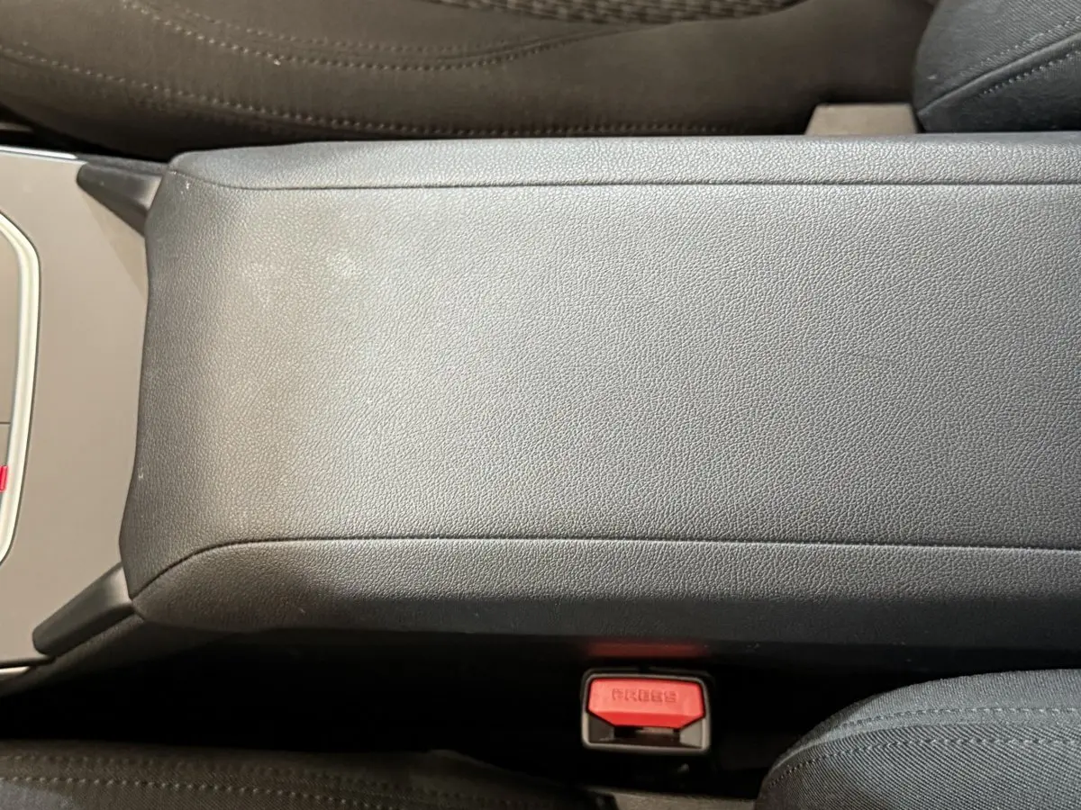 Gros plan sur l'accoudoir central gris et la boucle de ceinture rouge dans l'habitacle d'une BMW Série 1 116i 2023.