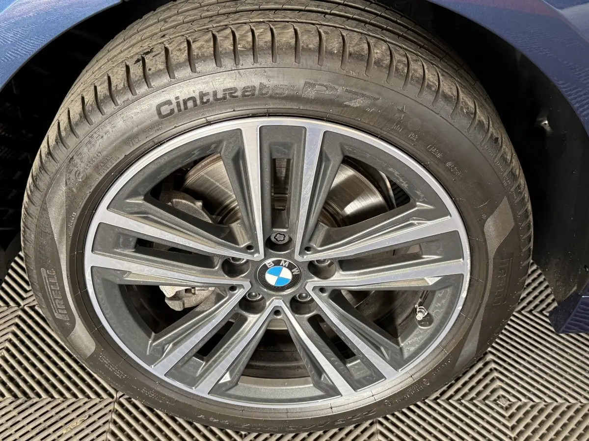 Gros plan sur la roue avant droite d'une BMW Série 1 bleu 116i avec jante alliage et logo central visible.