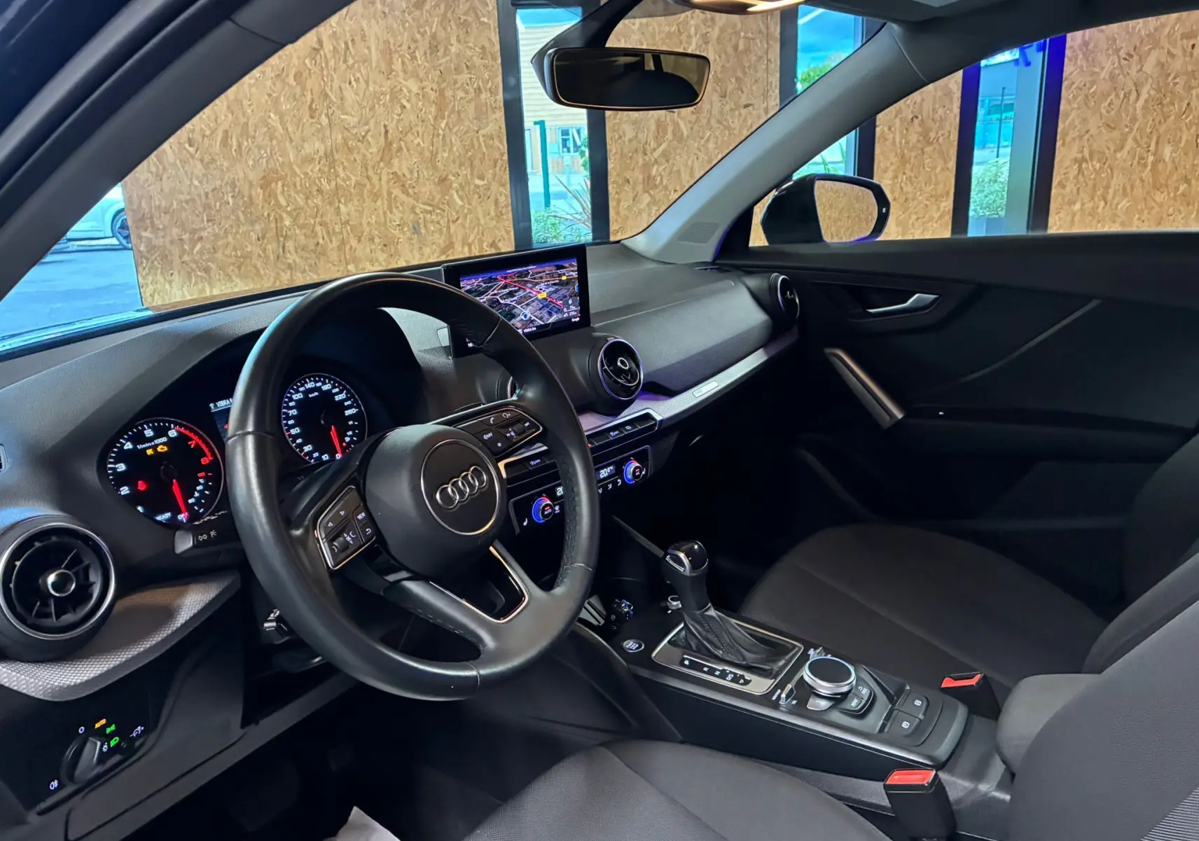 Intérieur noir de l'Audi Q2 35 TFSI 2023 vu côté conducteur, avec tableau de bord digital et écran GPS central.