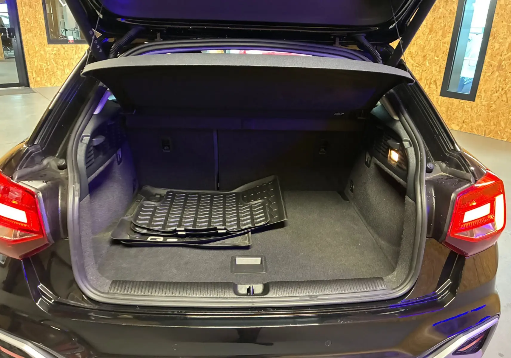 Coffre ouvert vu de l'arrière d'un Audi Q2 noir 35 TFSI S-Line 2023 avec tapis de sol à l'intérieur.