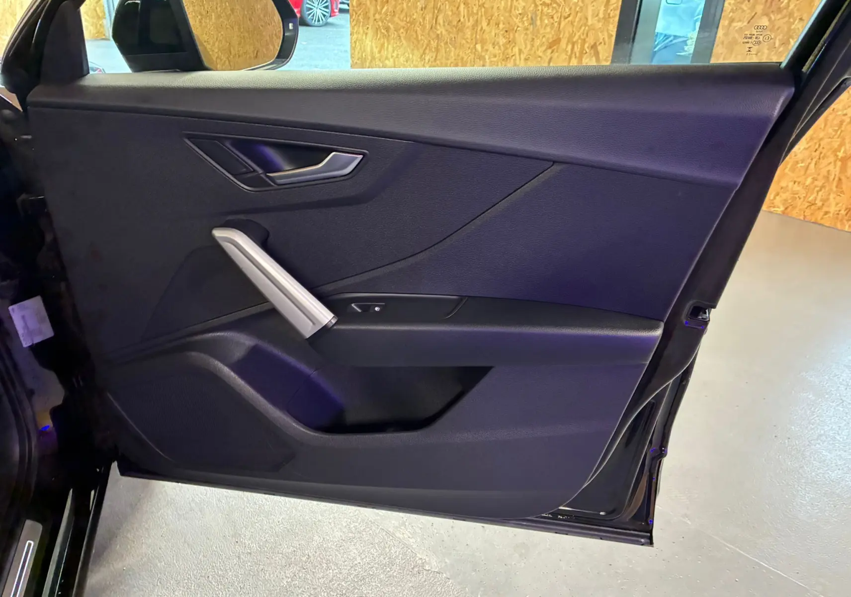 Vue intérieure de la porte avant gauche noire de l'Audi Q2 35 TFSI S-Line avec poignée argentée et garniture noire.