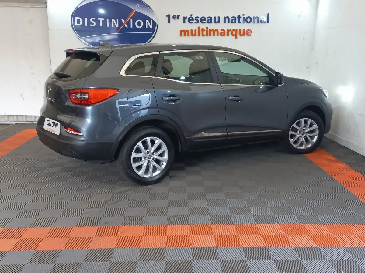 Vue côté droit d'un Renault Kadjar Business gris foncé 2022, avec jantes alliage et feux arrière visibles en intérieur showroom.