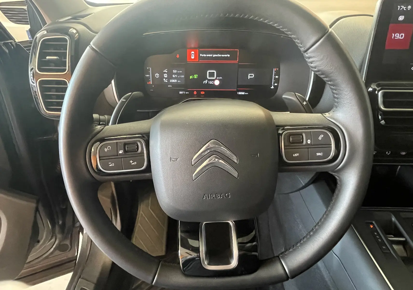 Vue rapprochée du volant en cuir noir du Citroën C5 Aircross Hybride 2025 avec commandes intégrées et tableau de bord digital.