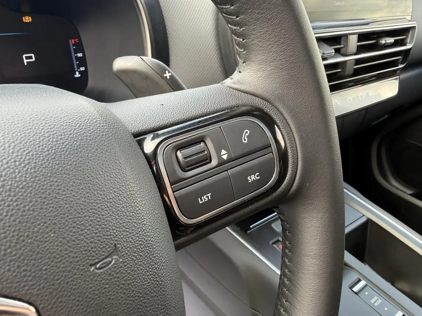 Gros plan sur la partie droite du volant en cuir noir du Citroën C5 Aircross 2024, avec commandes audio et tableau de bord numérique.