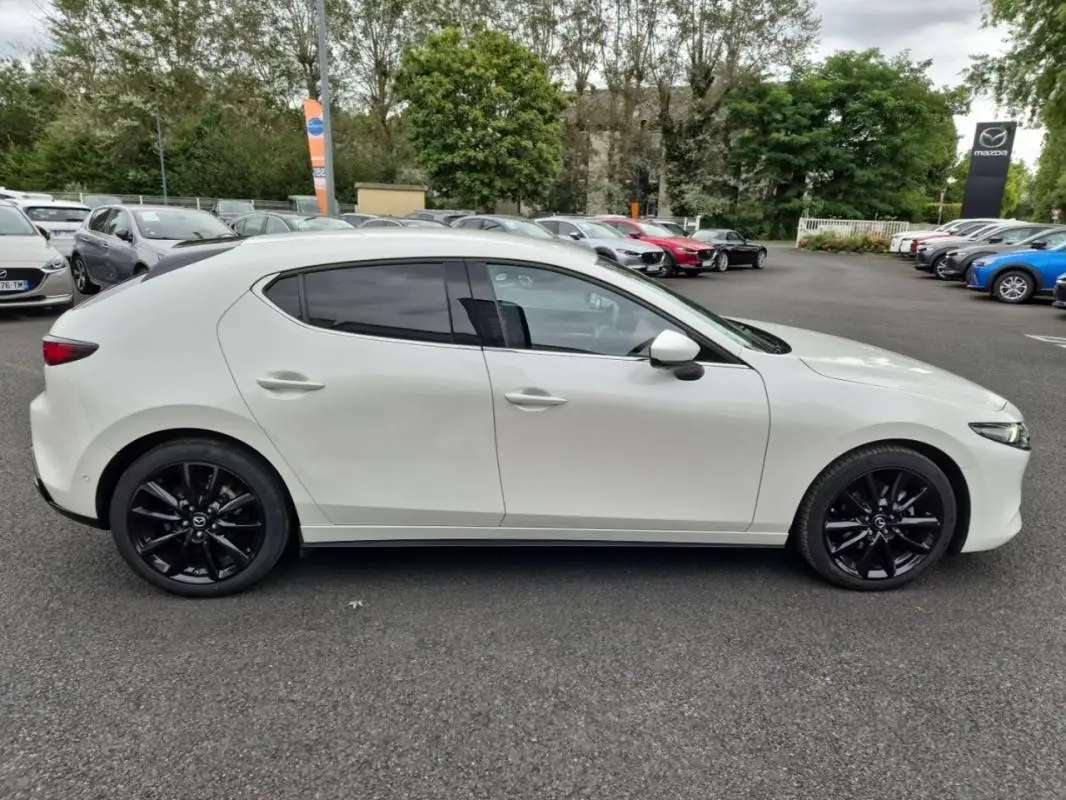 Vue de profil côté gauche d'une Mazda3 blanche de 2020 avec jantes noires sur un parking extérieur.