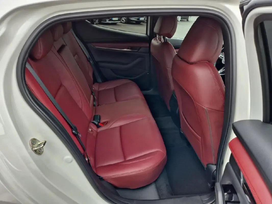 Vue intérieure côté gauche arrière d'une Mazda3 2020 blanche avec sièges en cuir rouge et garnitures assorties.