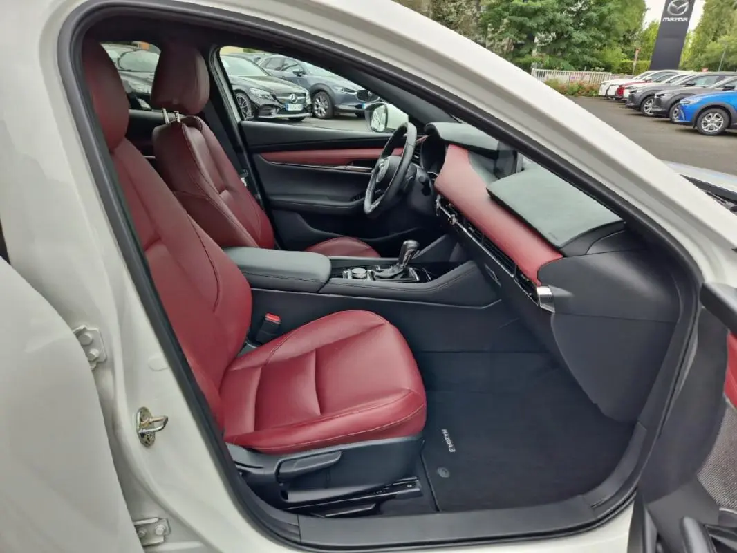 Vue intérieure côté conducteur d'une Mazda3 blanche 2020 avec sièges et tableau de bord en cuir rouge.