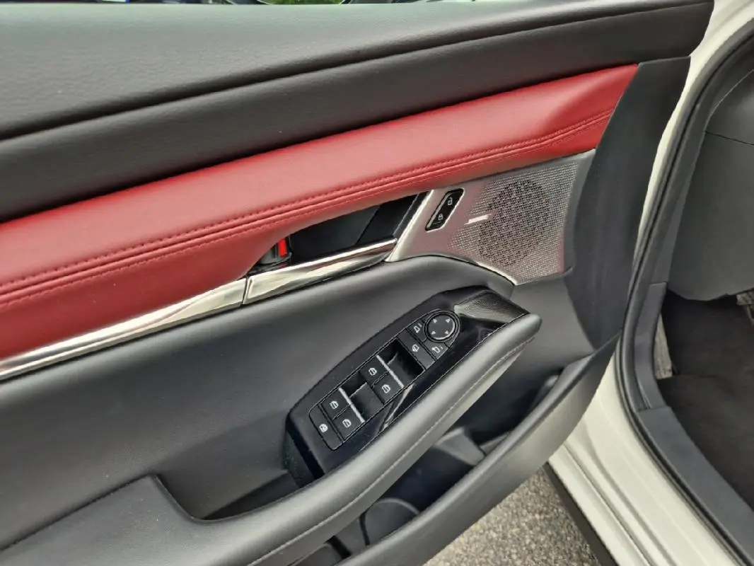 Détail de la porte avant gauche d'une Mazda3 blanche 2020, avec garniture cuir rouge et commandes électriques.