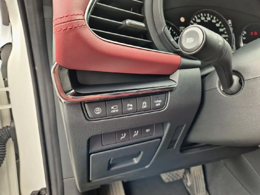 Gros plan sur les commandes sous le tableau de bord côté gauche d'une Mazda3 blanche avec garniture cuir rouge.