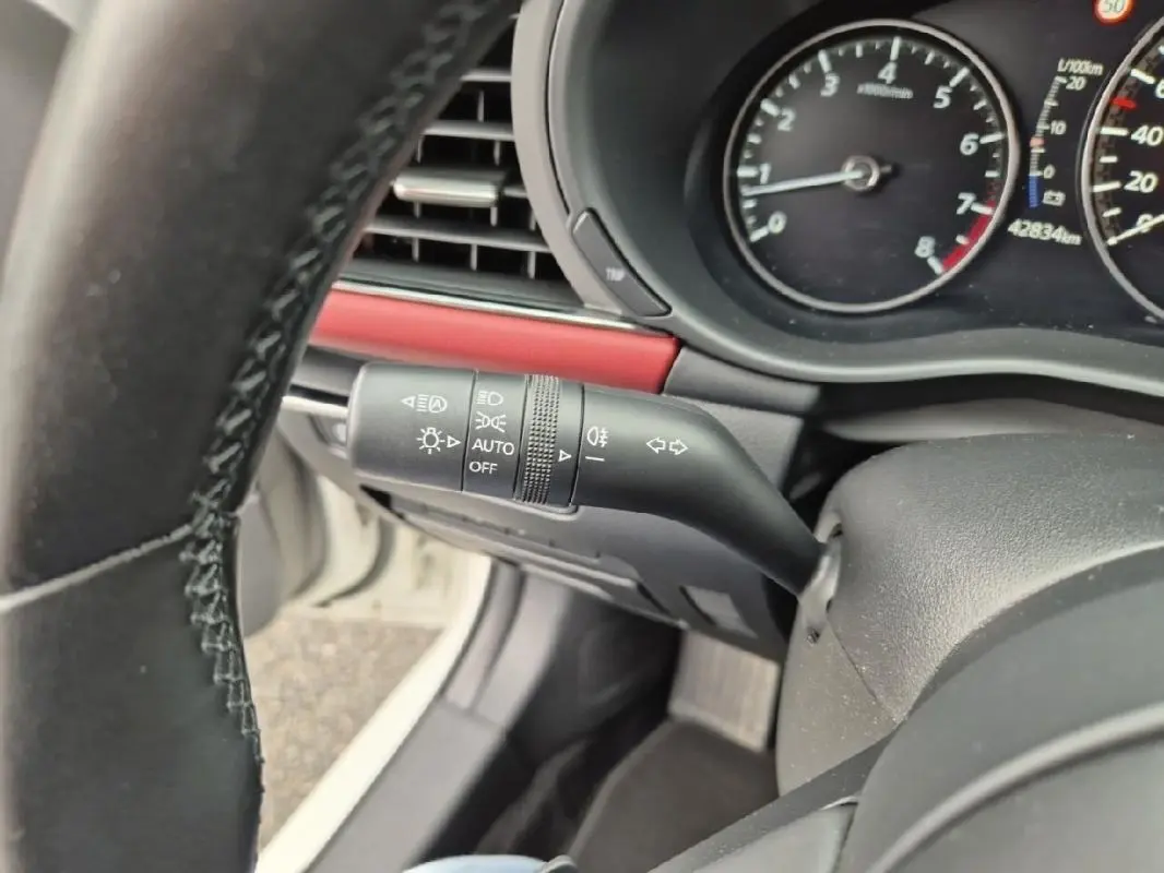 Gros plan sur la manette des feux et clignotants à gauche du volant d'une Mazda3 blanche, avec tableau de bord visible.