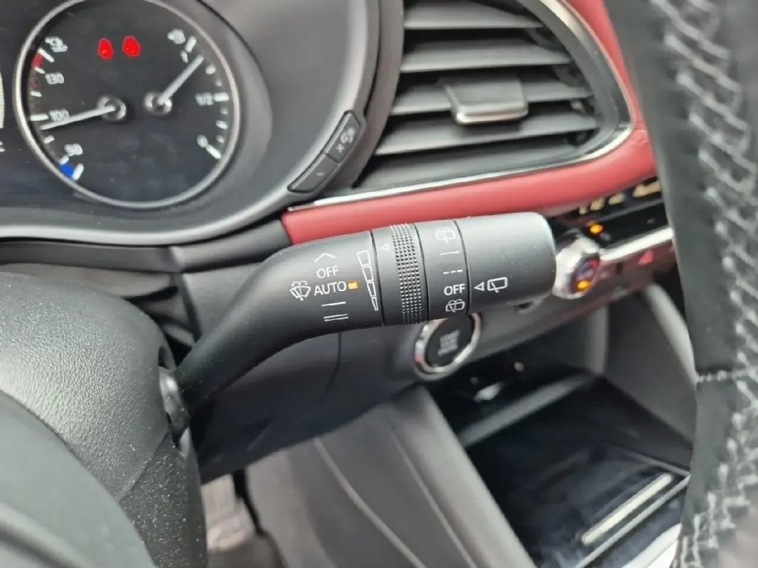 Gros plan sur la commande d'essuie-glace à gauche du volant dans l'habitacle rouge et noir d'une Mazda3 blanche de 2020.