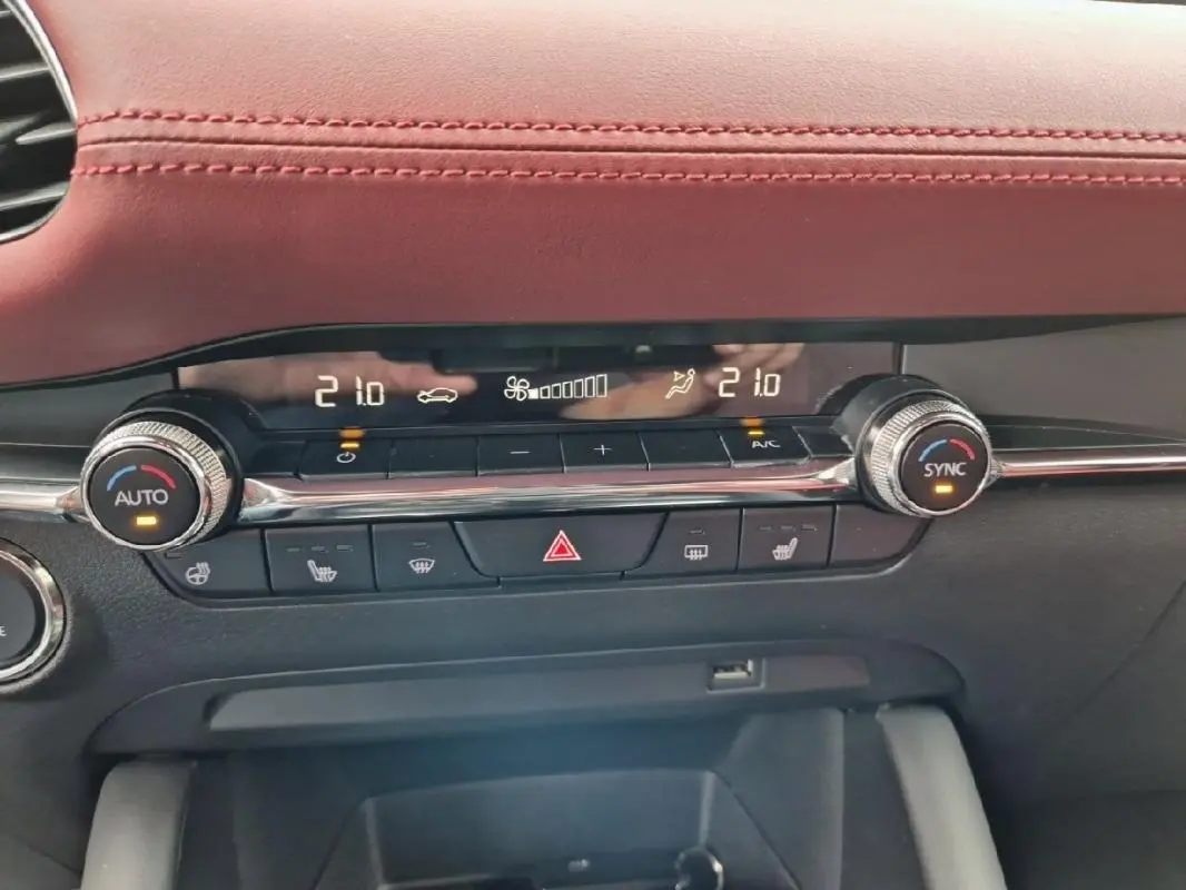 Vue rapprochée de la console centrale de la Mazda3 2020, mettant en valeur la climatisation digitale et le cuir rouge du tableau de bord.