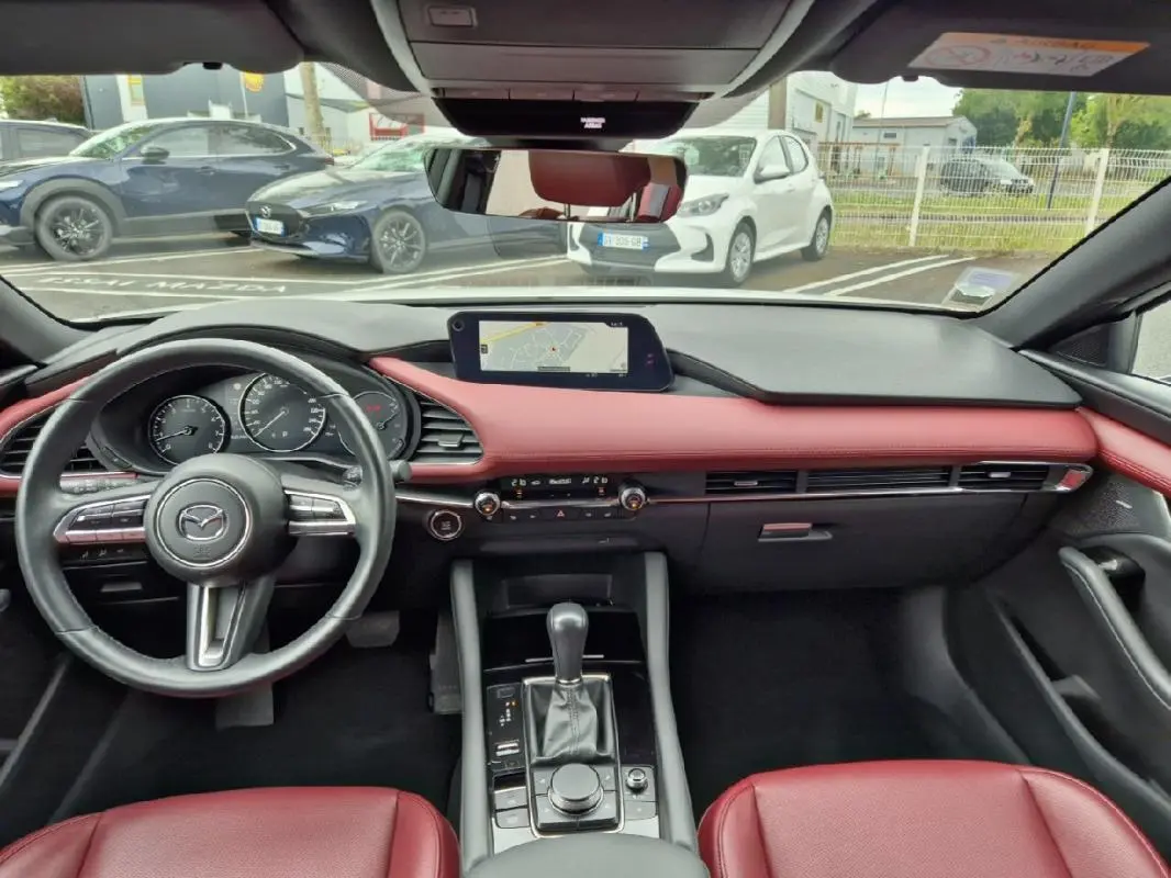 Vue intérieure du tableau de bord et console centrale d'une Mazda3 2020 avec sellerie cuir rouge et écran GPS intégré.