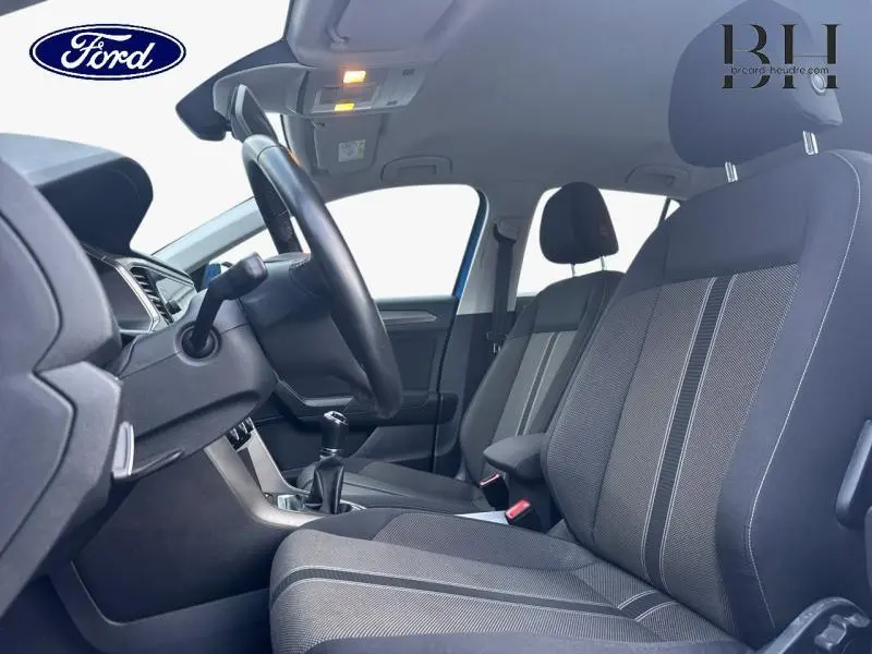 Vue intérieure côté conducteur du Volkswagen T-Roc bleu Ravenna, montrant les sièges tissu et le volant multifonction cuir.