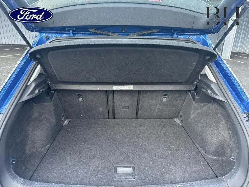 Coffre ouvert d'un Volkswagen T-Roc bleu Ravenna métallisé, vue de l'arrière montrant l'espace de chargement vide.