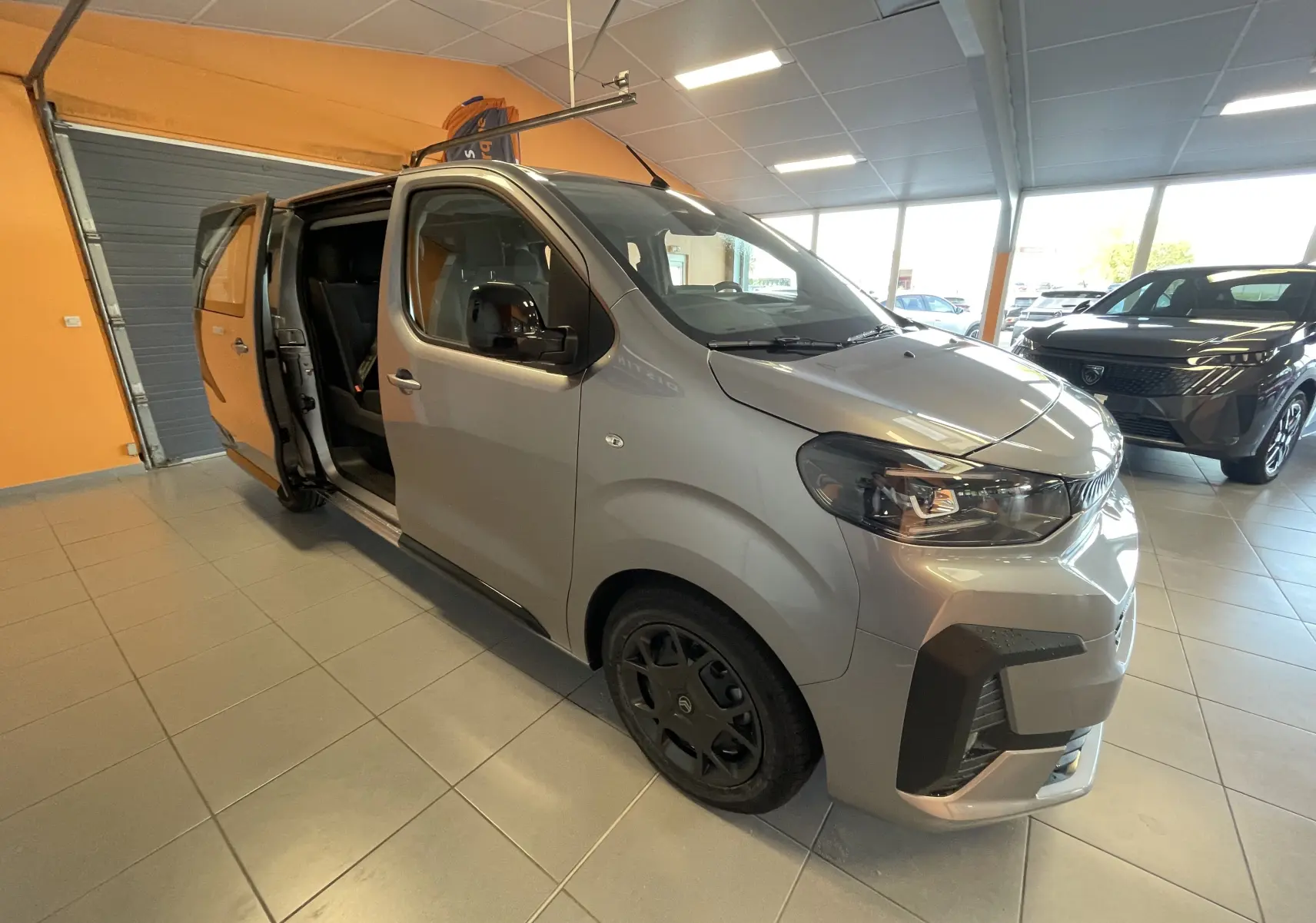 Vue 3/4 avant droit du Citroën Jumpy Cabine Approfondie gris Artense avec porte latérale coulissante ouverte en intérieur showroom.