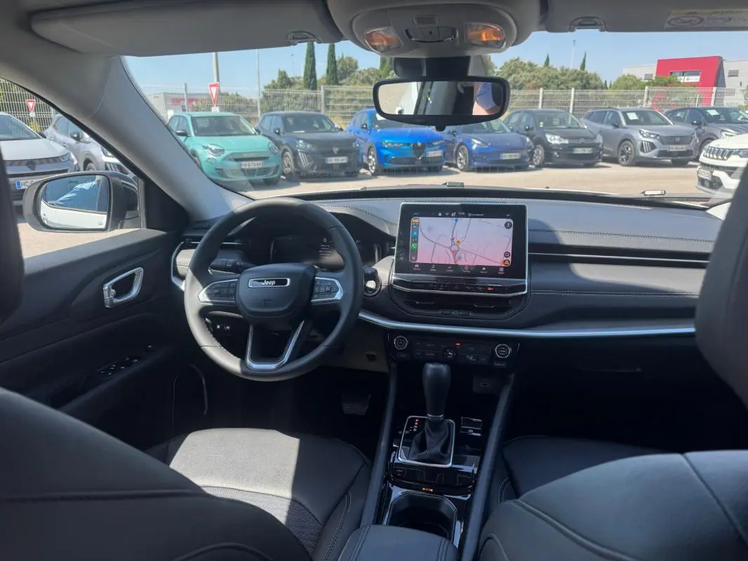 Vue intérieure avant du Jeep Compass 2025 avec tableau de bord noir et écran tactile central allumé.