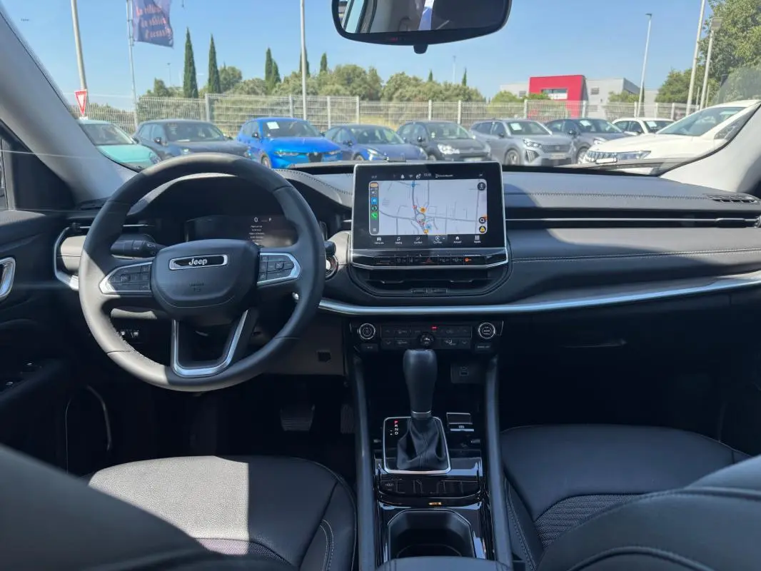 Vue intérieure avant du Jeep Compass blanc 2025, mettant en valeur le volant, l'écran tactile central et la console de boîte automatique.