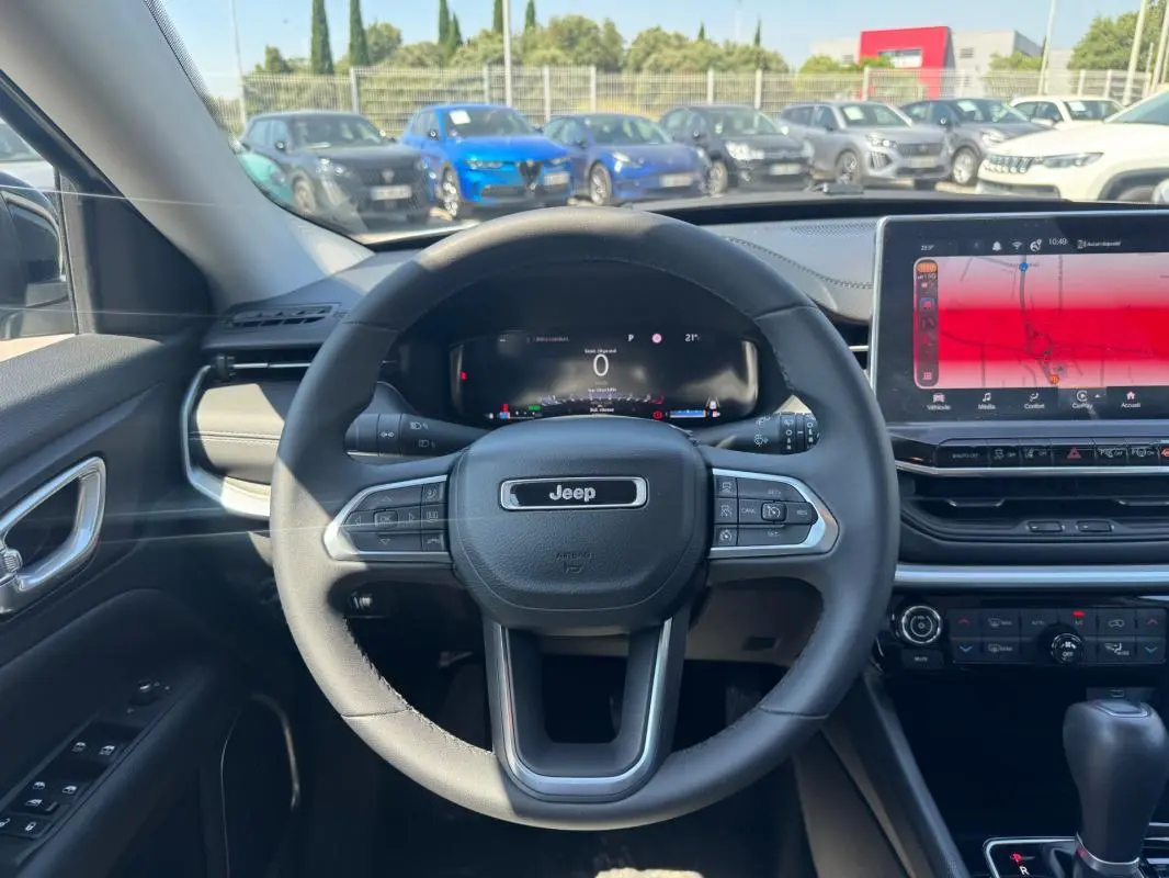 Vue intérieure centrée sur le volant Jeep d'un Compass blanc 2025, avec tableau de bord numérique et écran tactile large.