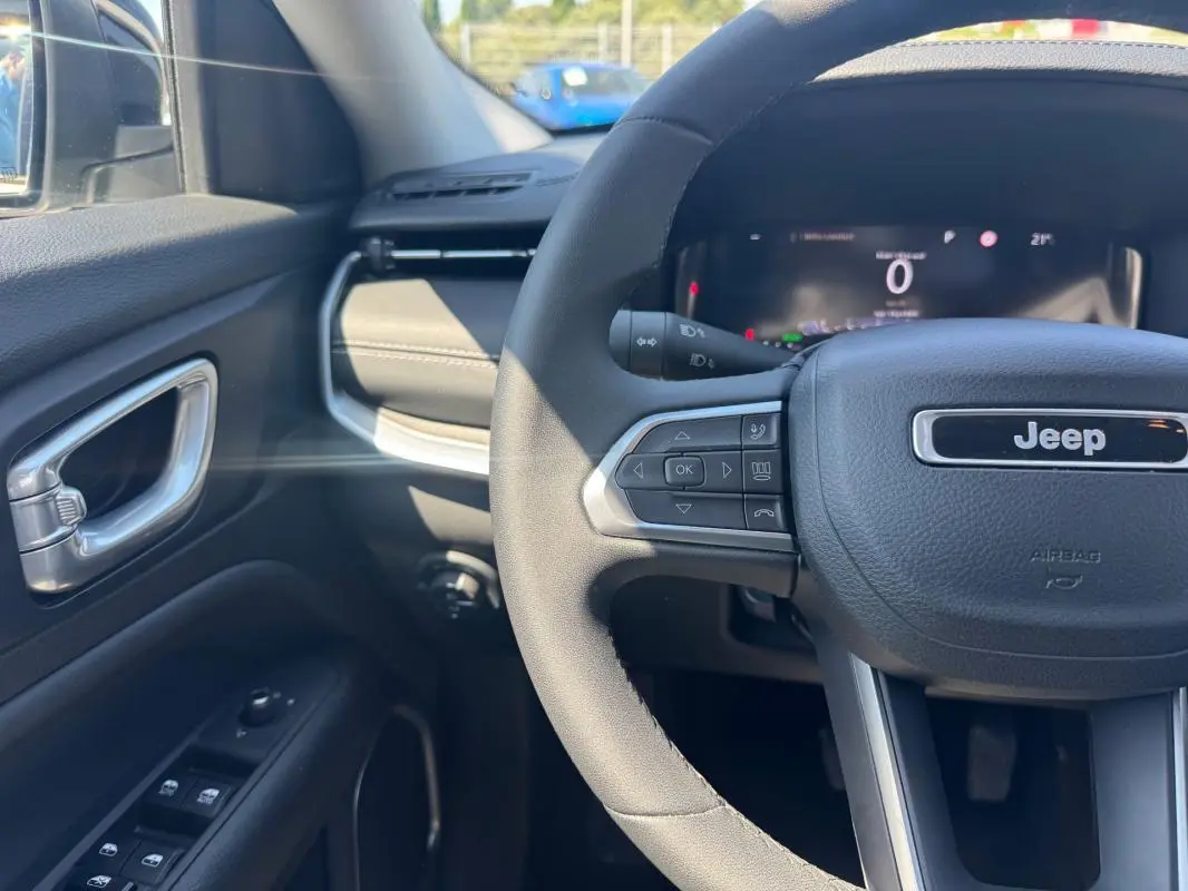 Vue rapprochée du volant et tableau de bord du Jeep Compass blanc, avec commandes au volant et affichage numérique.