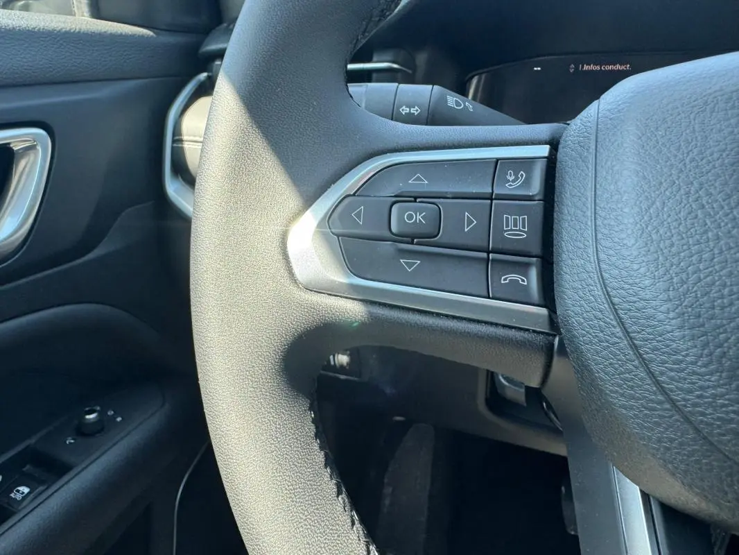 Gros plan sur le volant noir de la Jeep Compass 2025 avec commandes multifonctions côté gauche et tableau de bord partiel.