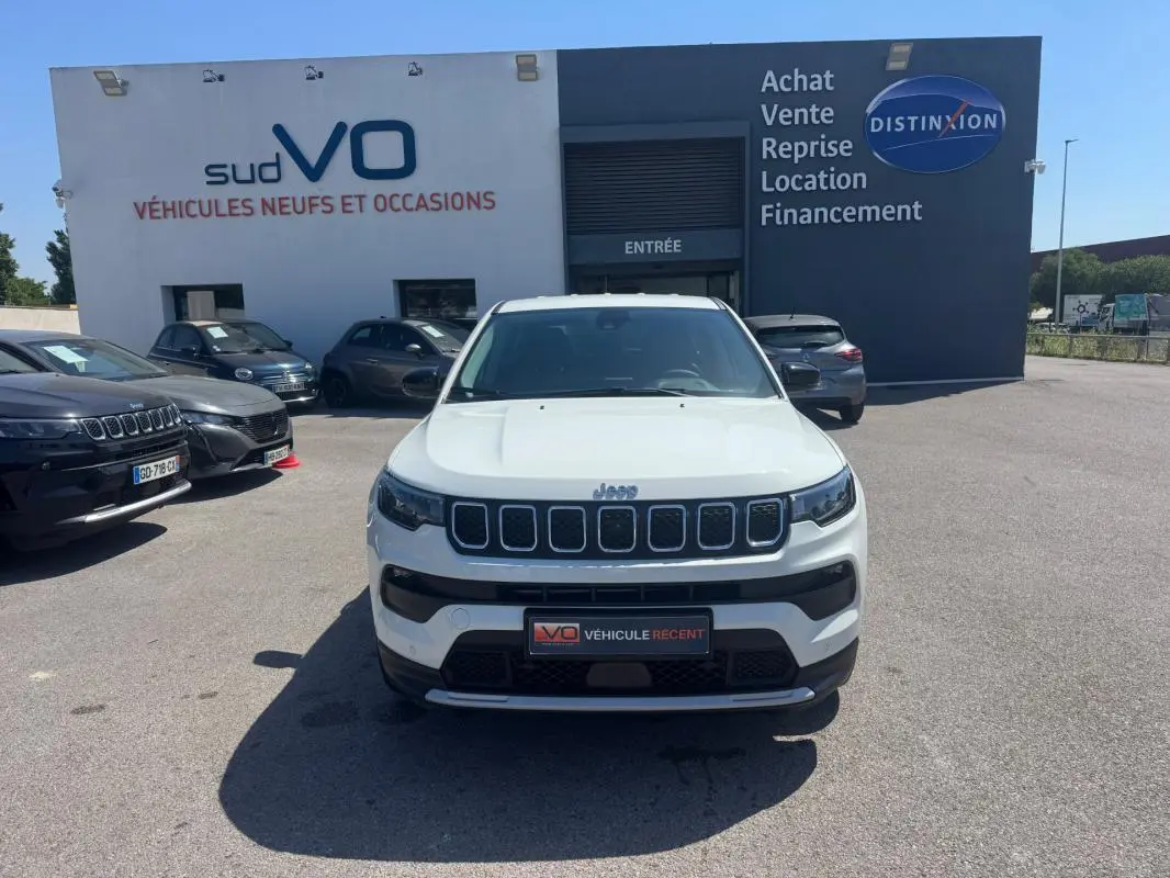 Jeep Compass blanc vue de face, calandre distinctive à sept fentes, stationné devant un bâtiment commercial.