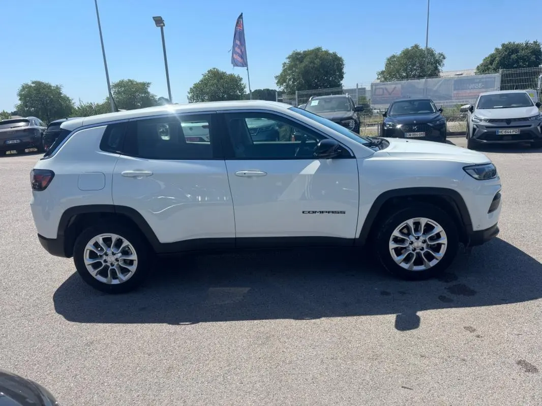 Vue de profil côté gauche d'un Jeep Compass blanc 2025 avec jantes alliage et logo "Compass" visible sur la porte.