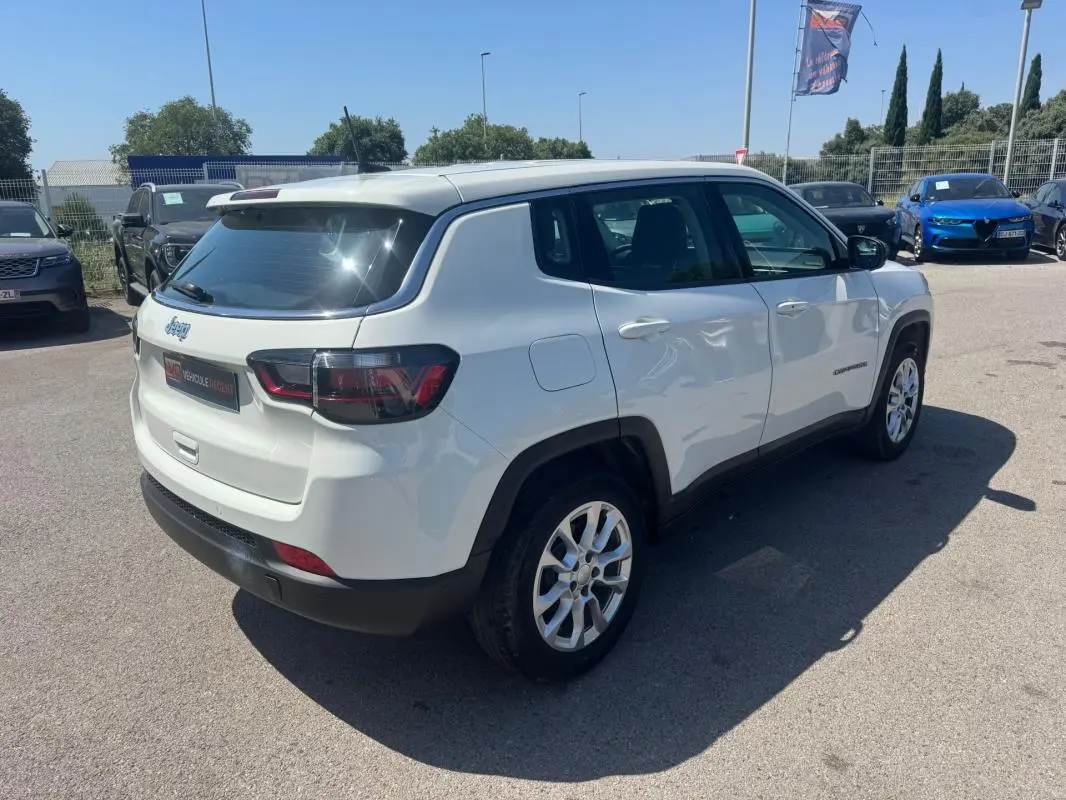 Jeep Compass blanc vue 3/4 arrière droit, avec jantes alliage et feux arrière LED visibles en plein jour.