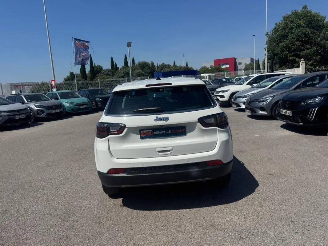 Vue arrière d'un Jeep Compass blanc 2025 garé en extérieur, avec feux arrière LED et logo Jeep bien visible.