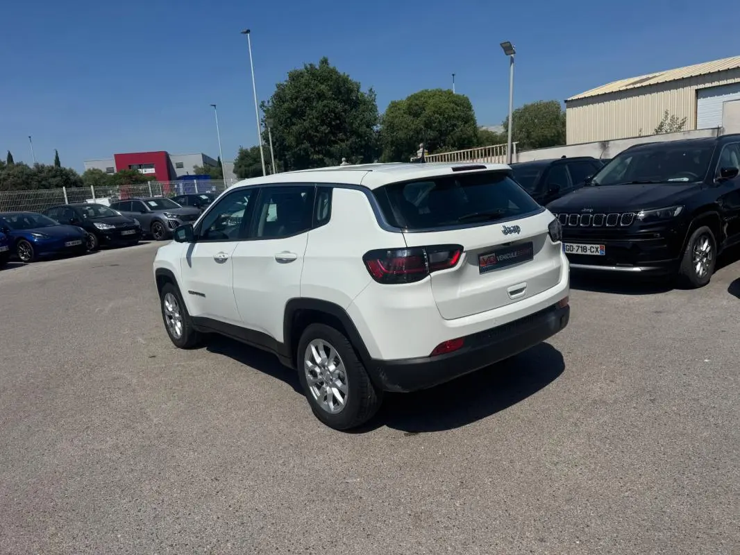 Vue 3/4 arrière droite d'un Jeep Compass blanc stationné en extérieur sous un ciel dégagé.