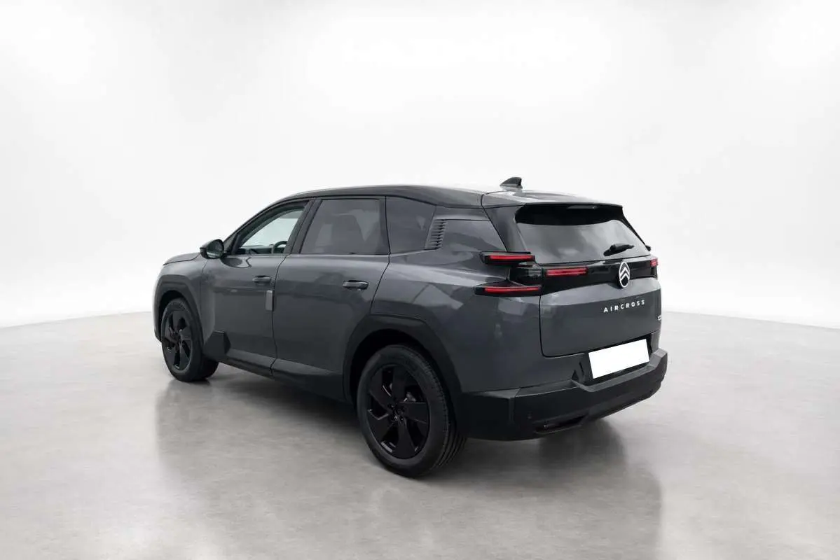 Vue 3/4 arrière gauche du Citroën C5 Aircross gris foncé avec toit noir et jantes noires dans un studio blanc.