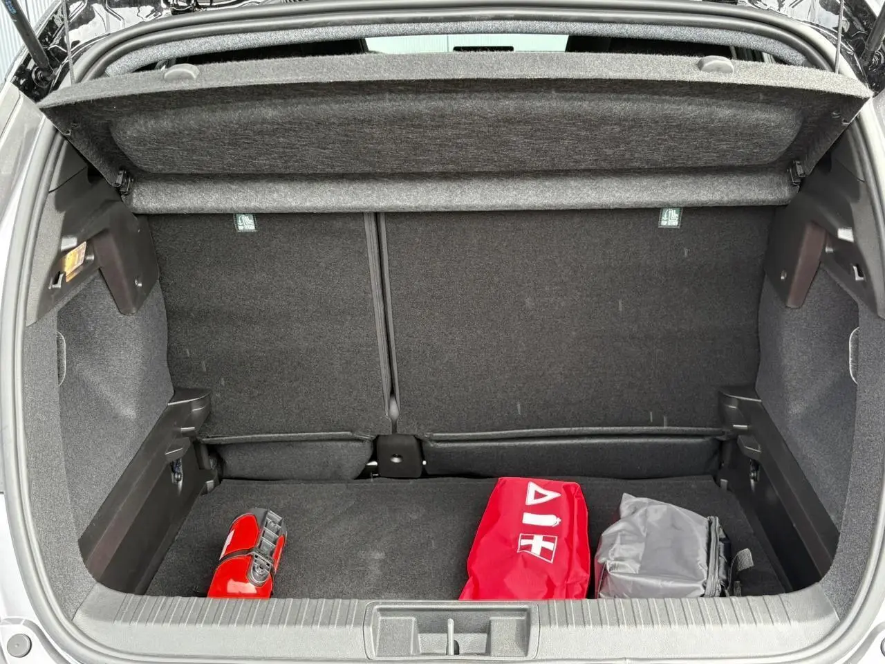 Coffre ouvert d'un Renault Captur Gris Cassiopée 2025, vue arrière montrant un kit de sécurité rouge et un sac gris.