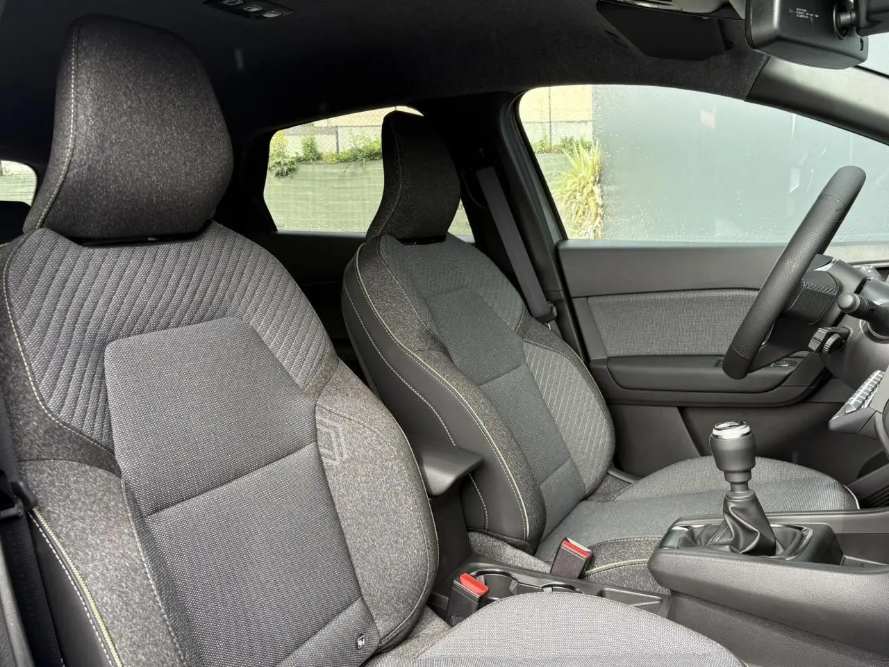 Vue intérieure côté conducteur du Renault Captur 2025, sièges gris avec coutures contrastées et levier de vitesse manuel.