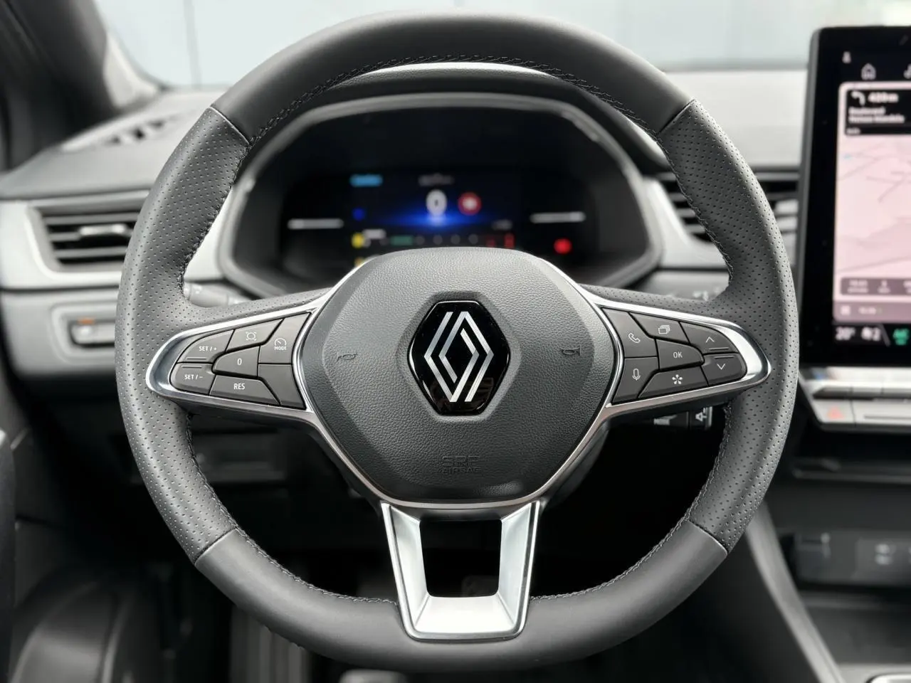 Vue rapprochée du volant cuir perforé du Renault Captur 2025 avec commandes intégrées et tableau de bord numérique flou.