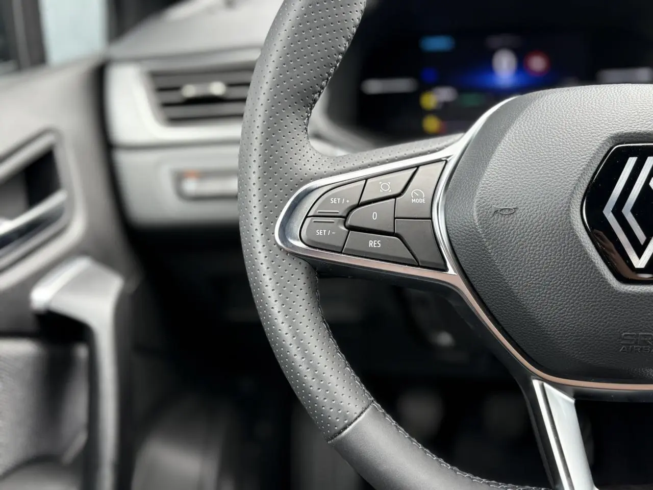 Gros plan sur le volant en cuir perforé du Renault Captur 2025 avec commandes intégrées et tableau de bord flou.