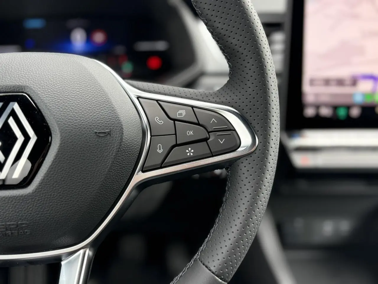 Gros plan sur le volant perforé du Renault Captur 2025 avec commandes intégrées et écran tactile flou en arrière-plan.