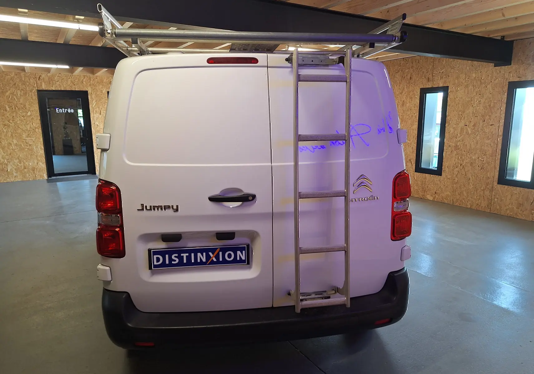 Vue arrière d'un utilitaire blanc Citroën Jumpy 2.0 BlueHDi 120 avec échelle métallique fixée sur la porte droite.