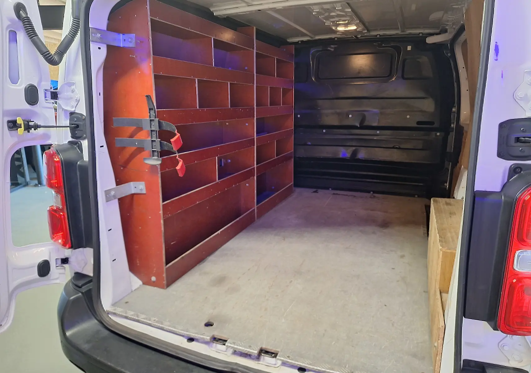 Intérieur arrière du Citroën Jumpy blanc 2020, montrant les portes ouvertes et des étagères en bois sur le côté gauche.