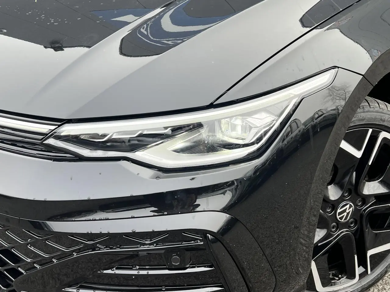 Gros plan sur l'avant droit noir brillant d'une Volkswagen Golf VIII R-Line avec phare LED et jante alliage 18 pouces.