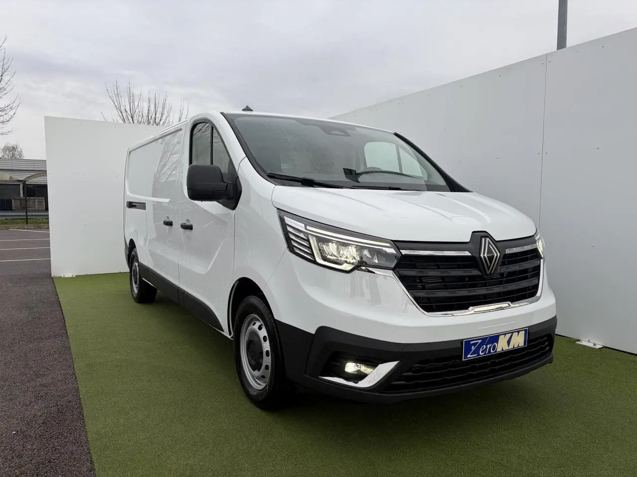Renault Trafic Fourgon blanc glacier vu en 3/4 avant droit, avec projecteurs LED allumés et jantes tôles 16 pouces.