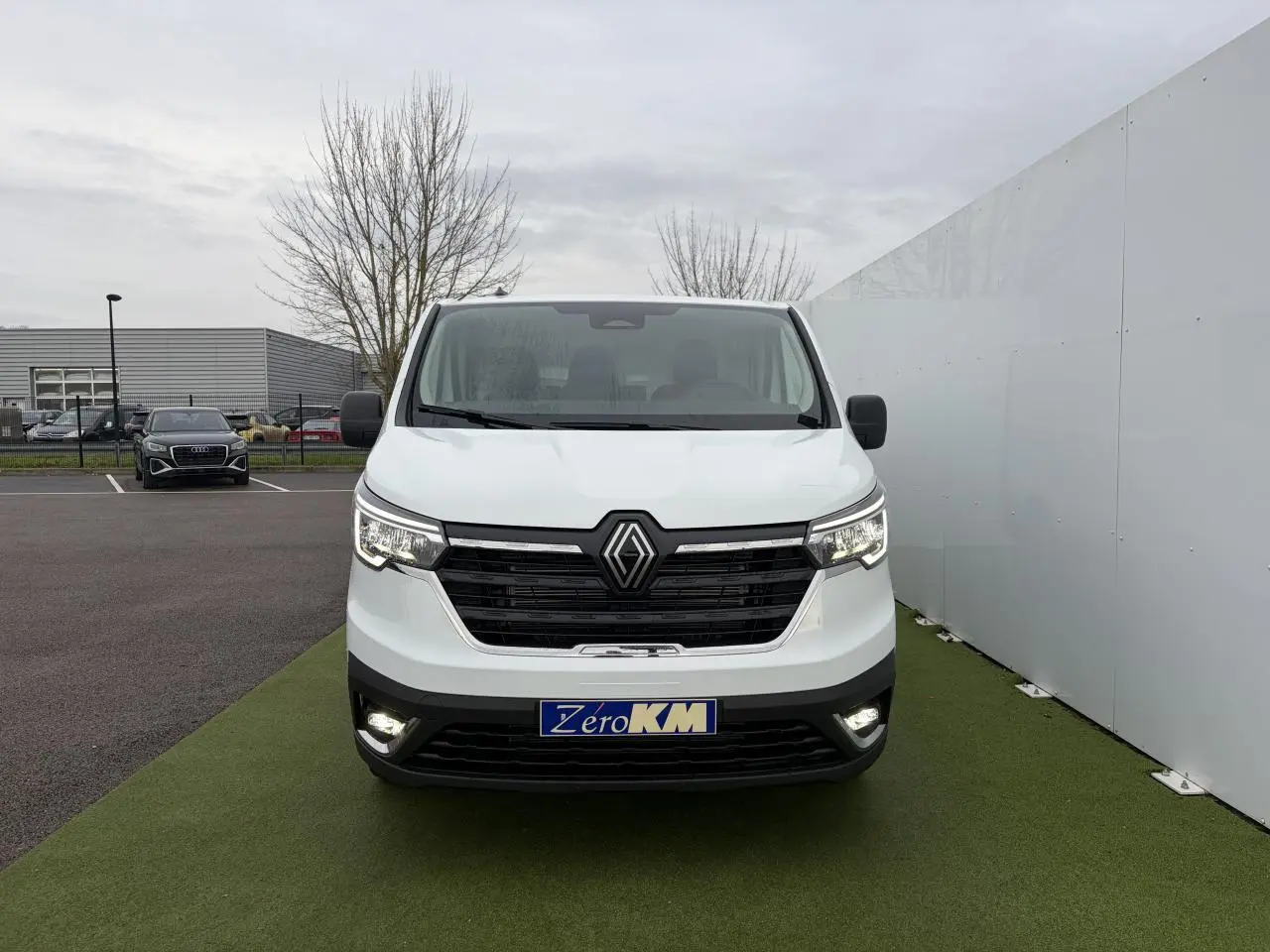 Vue frontale d'un Renault Trafic Fourgon blanc Glacier avec feux LED allumés sur un sol vert synthétique.
