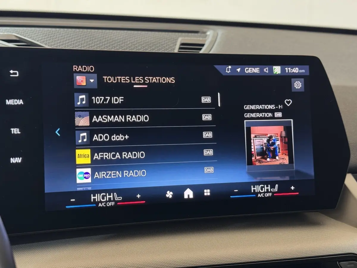 Écran tactile central affichant les stations radio dans l’habitacle beige d’une BMW X1 gris foncé, vue de face.