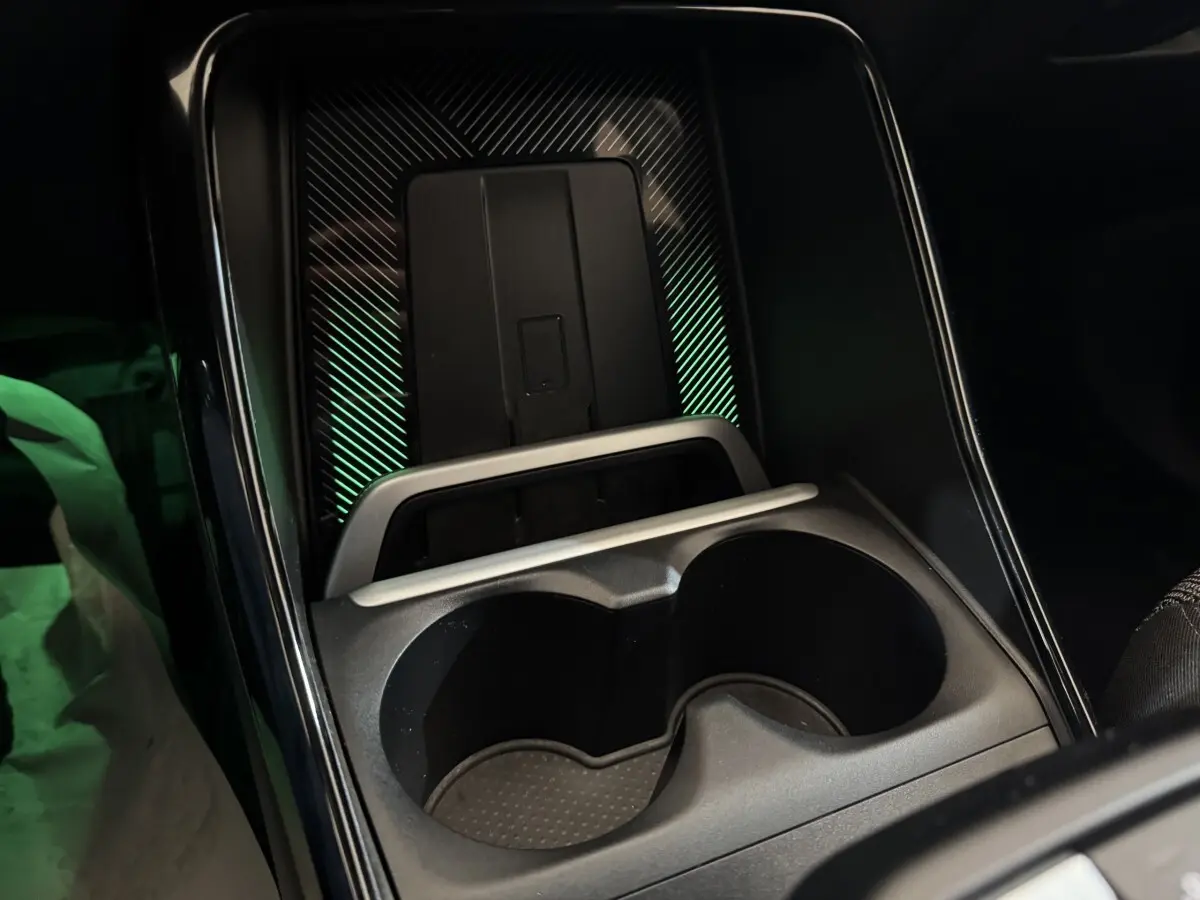 Gros plan sur la console centrale noire du BMW X1 2024 avec porte-gobelets et zone de recharge à induction éclairée.